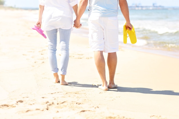 couple walking at the beach and carrying flip flops