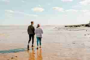 Photo a couple walking on the beach of hopewell rocks park on a sunny day against the blue cloudy sky