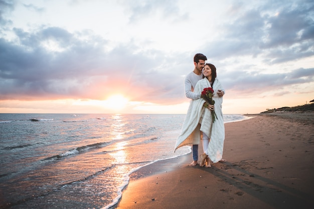 Foto coppia camminare sulla spiaggia con un mazzo di rose al tramonto