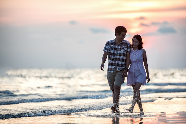 Couple walking on beach. Young happy interracial couple walking on beach smiling holding around each