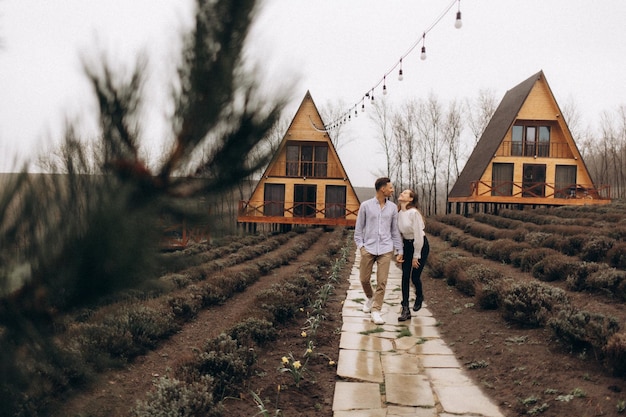 A couple walks in front of a house with a string of lights hanging from the roof.