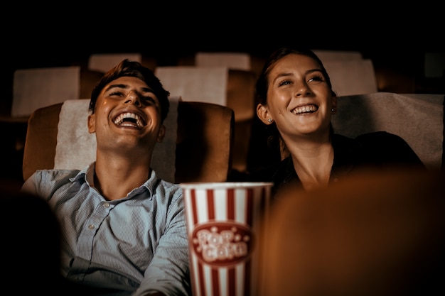 Пара смотрит фильм в театре с попкорном и счастливым лицом