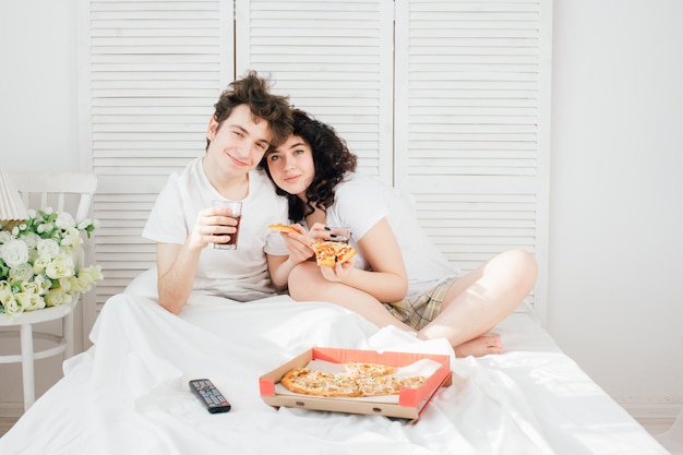 Couple watching TV in bed and eating pizza