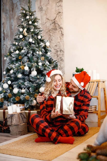 床に座っているクリスマスの格子縞の赤いパジャマを着ているカップル