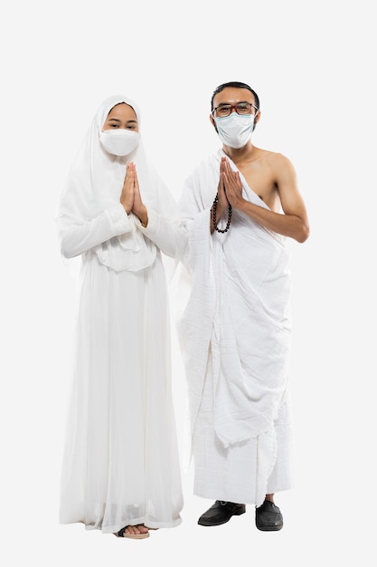 Premium Photo | Couple wearing hajj ihram clothes and masks with greeting  gesture standing on isolated background
