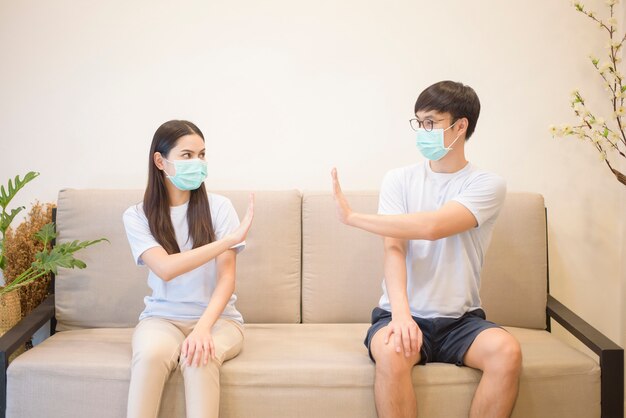 A couple wearing a mask is sitting on a sofa at home during quarantine for protection and avoiding from coronavirus