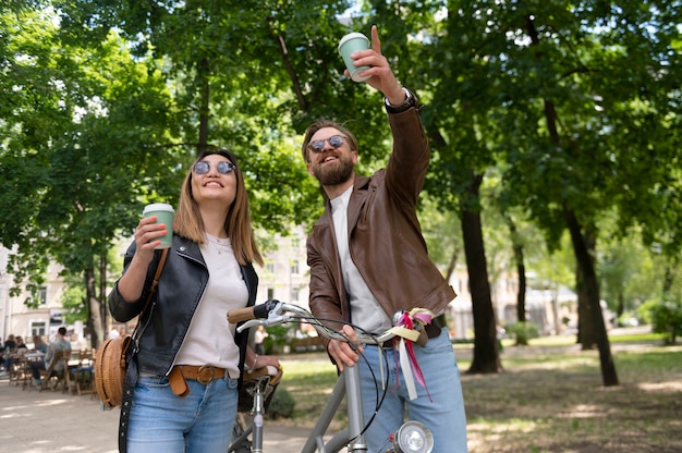 Couple wearing synthetic leather jackets having coffee together outdoors while riding bikes