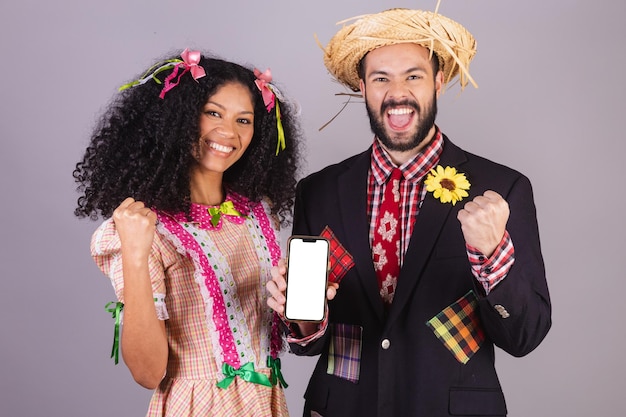 Foto coppia che indossa abiti tipici della festa junina arraial festa de sao joao con smartphone in mano