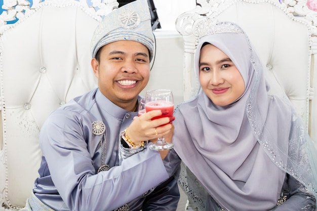 Photo a couple in a wedding dress and a man in a blue suit are sitting on a couch and drinking a glass of red wine.