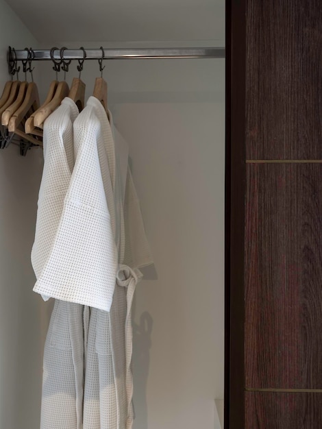 객실 수직 스타일의 호텔 투숙객을 위한 나무 옷장 내부의 선반에 있는 나무 옷걸이에 흰색 깨끗한 목욕 가운 몇 개