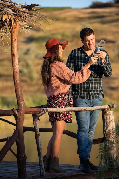 Couple of wine tasters looking at the color of the wine on a wooden pontong by the edge of a lake