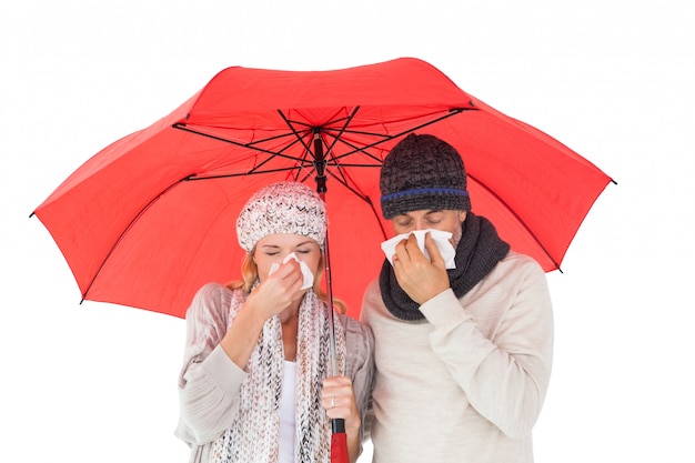 Couple in winter fashion sneezing under umbrella