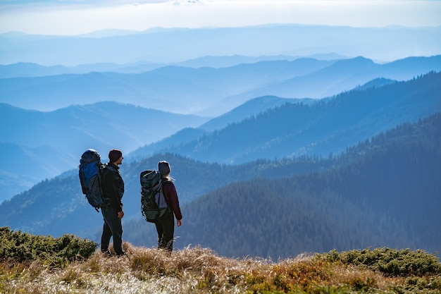 The couple with backpacks standing on the mountain with a beautiful view