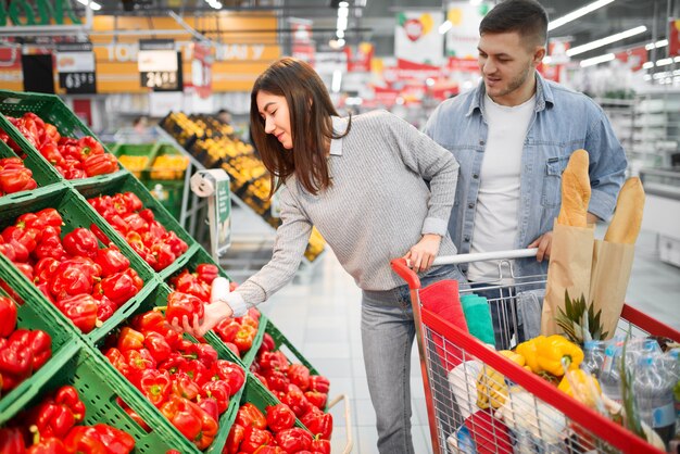 Coppia con carrello scegliendo peperoni rossi dolci freschi in un supermercato