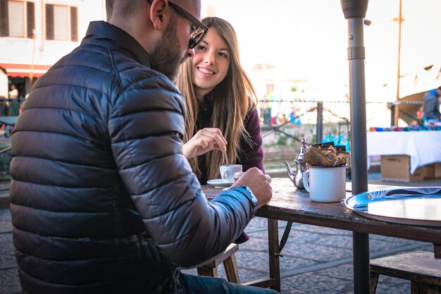 写真 外のカフェに座ってテーブルでコーヒーを飲んでいるカップル