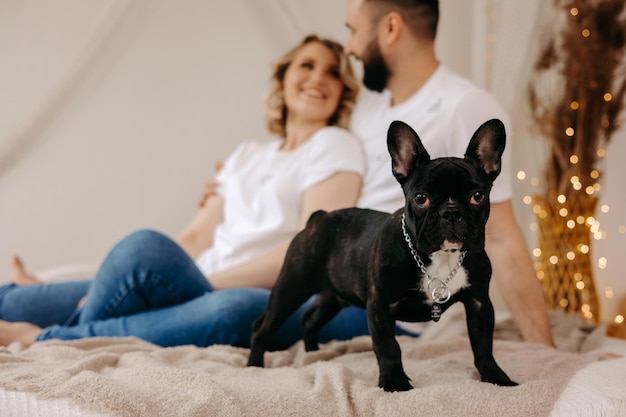 犬とのカップルフレンチブルドッグはベッドにいますフレンチブルドッグはカメラに見えます