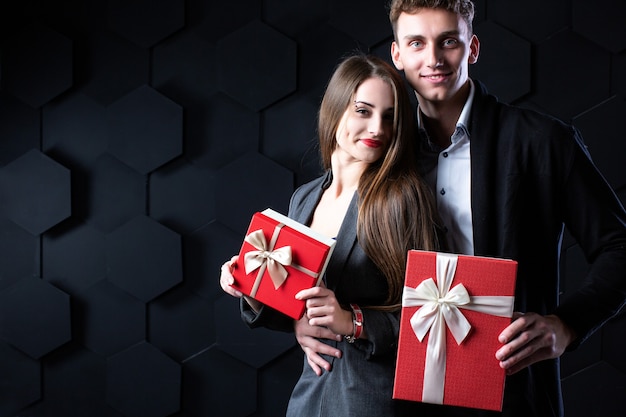 Couple with gifts. Beautiful man and woman holding gift boxes on a dark background. Celebration and romantic concept.