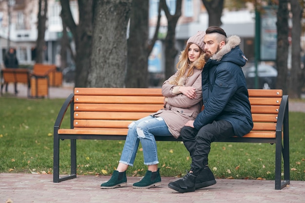 couple with jacket in park sits on a bench