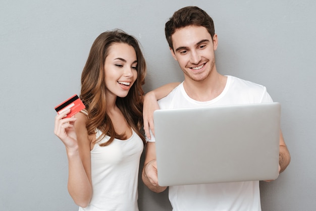 Couple with laptop and credit card . Isolated gray wall