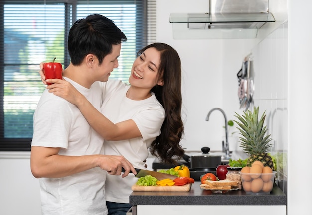 家の台所で一緒に料理する野菜を準備するカップルと女性は男を抱き締めています