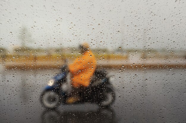 A couple with raincoat on a motorbike during hard rainfall. Selective focus and very shallow depth of field composition.