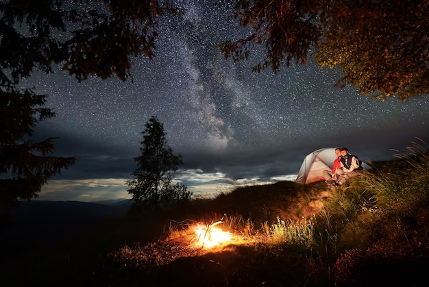 Photo couple with a tent sitting next to a bonfire