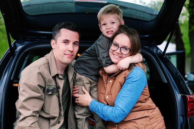 Couple with their young son in  open trunk of  off-road vehicle in  parking