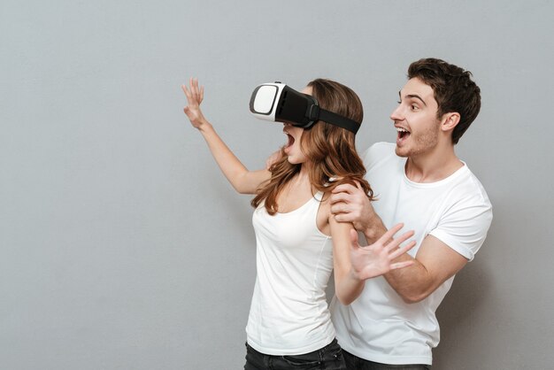 Couple with virtual reality device . Woman using device and man standing from the her back. Isolated gray wall