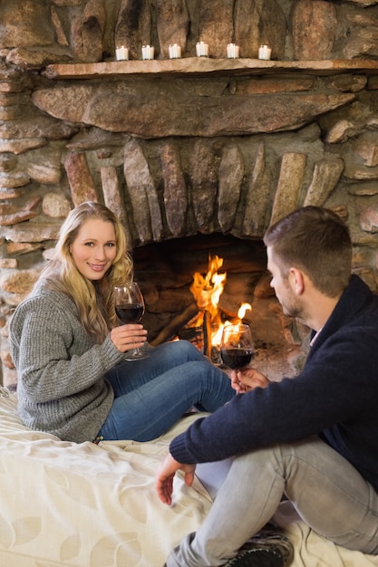 Couple with wineglasses in front of lit fireplace