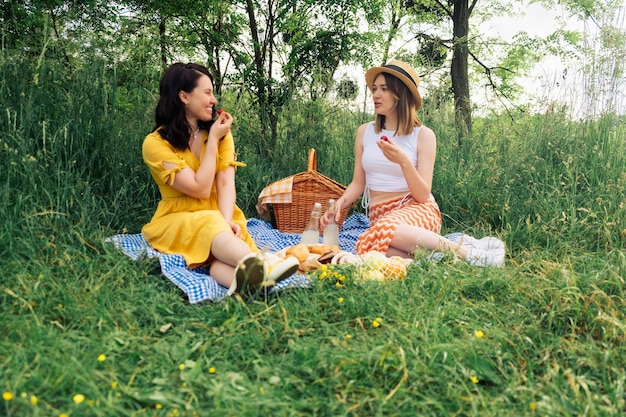 A couple of women chatting while sitting on blue picnic blanket in open air