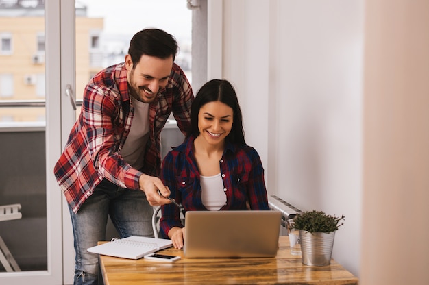 Couple working together in apartment, man pointing on computer