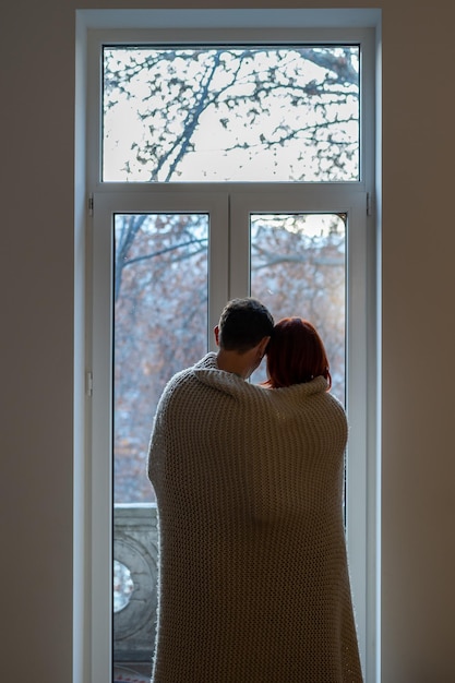 Couple wrapped in blanket looking out window