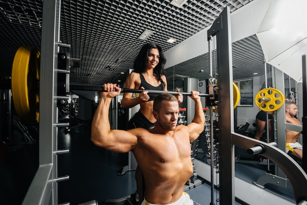 A couple of young athletes are engaged in the gym helping each other. Fitness, bodybuilding.