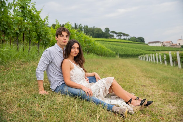 Couple of young boy and girl in love sitting on the grass in the vineyard enjoying life