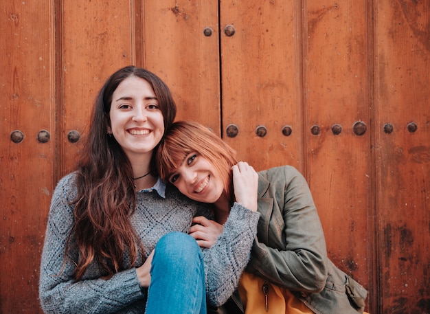 Couple of young girls sitting at the door while looking at the camera and being happy