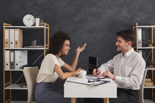 Couple of young happy business partners working in modern office. Laughing man and woman discussing new project and having fun while drinking coffee, copy space