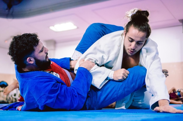 A couple of young latino and hispanic men with beards practicing jiujitsu in a gym Selfdefense