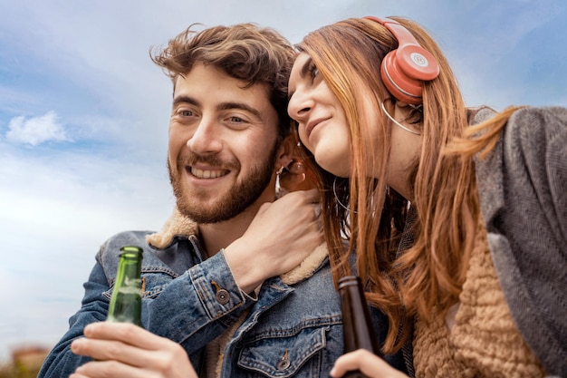 Пара молодых любителей, слушающих музыку, делясь беспроводными наушниками на открытом воздухе