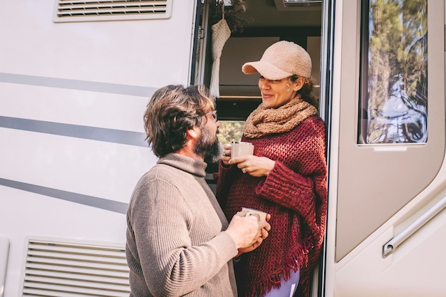 Couple of young mature people enjoy time talking outside the door of a modern camper van during summer holiday travel vacation Man and woman together living on a motor home with nature outdoors