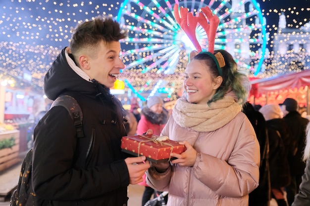 クリスマスマーケットの若者のカップル。幸せな休日の男の子と女の子のギフトボックスを与える