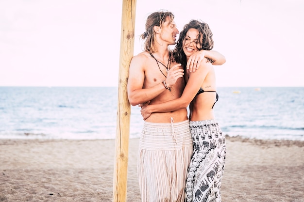 couple of young pretty male and female hug eachother at the beach under an umbrella sun