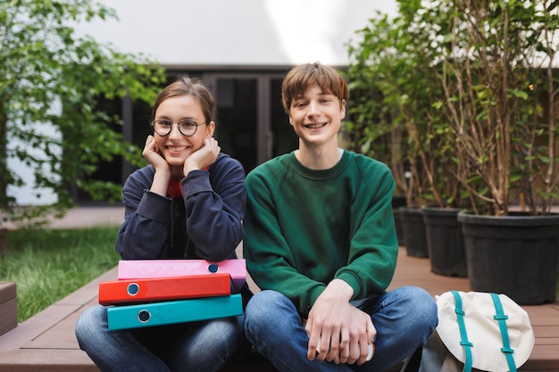 Couple of young smiling students sitting with colorful folders and happily 