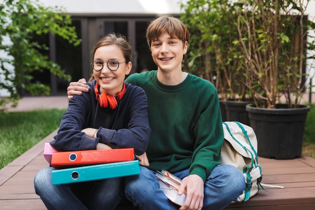 Foto coppia di giovani studenti seduti con cartelle e libri in mano e con gioia