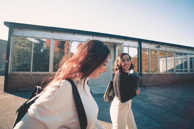 Couple of young woman student of college walking through the
campus. they walks trough university campus and laughing after
meeting again at the university. study together and learning
concept. trendy