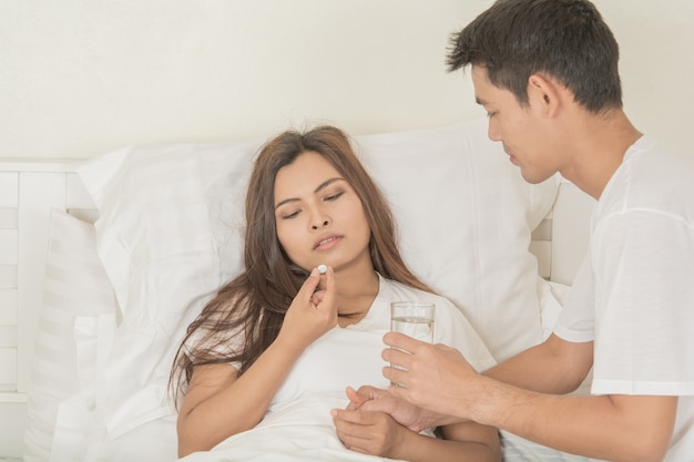Couples  give medicine  sick woman and glass of water in hand  on bed