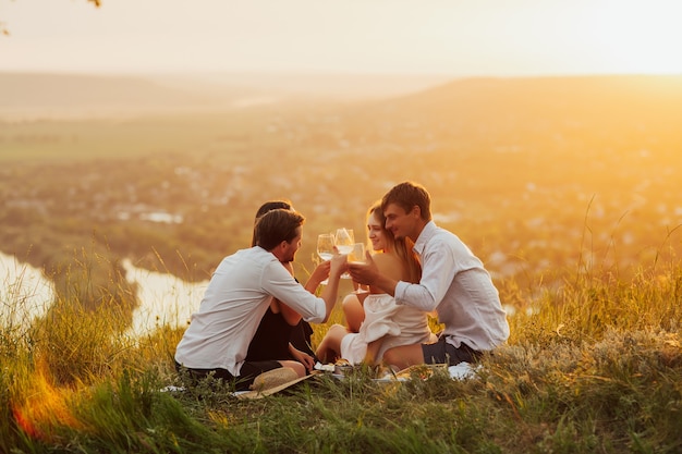 Couples having a picnic in the countryside. People with glasses of white wine on the surface of river at the picnic.