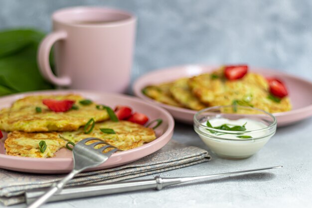 Courgette beignets, vegetarische courgette beignets, geserveerd met verse kruiden en zure room. Gegarneerd met aardbeien en groene uien. Op een lichtgrijze tafel.