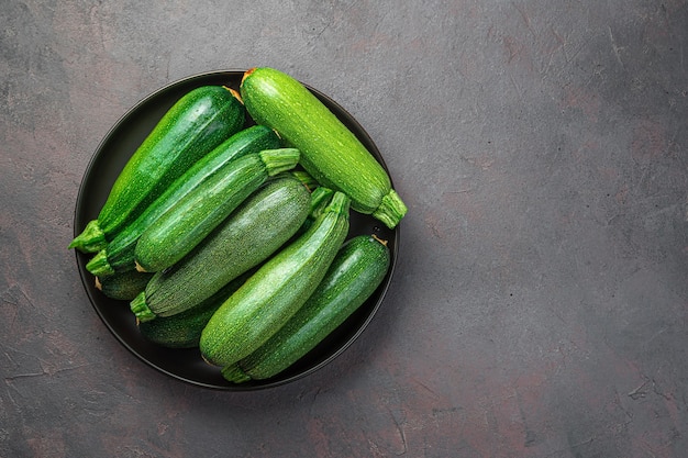 Courgette in een zwarte plaat op een grijsbruine achtergrond. Bovenaanzicht, kopieer ruimte.