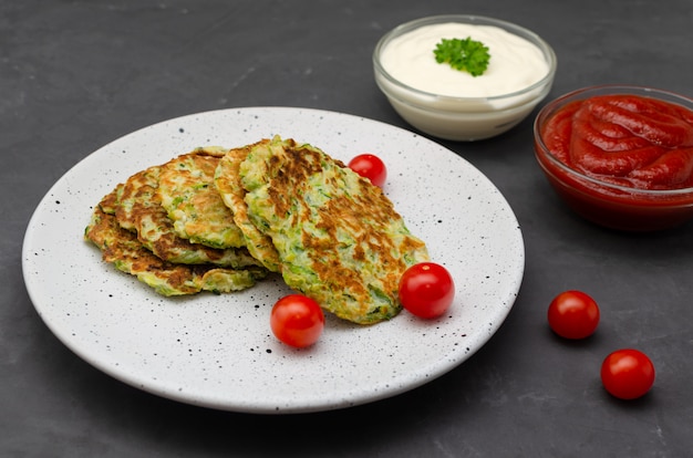 Courgettepannekoeken met groenten, geserveerd met yoghurt en tomatensaus. op donkere tafel. close-up weergave.