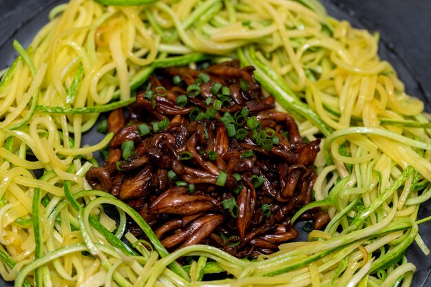 Courgettespaghetti met shimeji op zwarte stenen plaat.